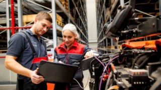 Dois técnicos de assistência da Linde Material Handling olham para um computador portátil junto a um equipamento.