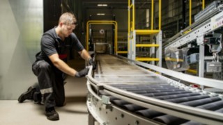 Um técnico de assistência da Linde MH repara um transportador de rolos