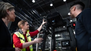 Três pessoas estão em frente a um equipamento automatizado da Linde MH.