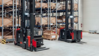 Dois empilhadores para corredores estreitos da Linde MH com sistema de proteção de pessoas integrado em frente a um armazém de corredores estreitos