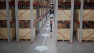 Animação de uma colaboradora com colete de proteção num armazém de corredores estreitos e das zonas de segurança para deteção de pessoas