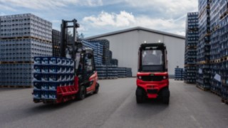 O Linde Reverse Assist Radar reconhece todos os obstáculos independentemente das condições de iluminação. Dois empilhadores elétricos da Linde estacionados no recinto exterior, entre grades de bebidas empilhadas.