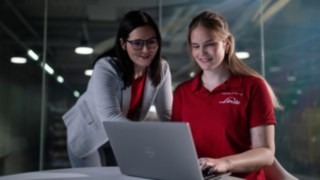 Duas pessoas estão sentadas em frente a um computador portátil.