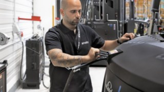 A fim de evitar picos de carga, o connect:charger da Linde estipula que os carregadores podem consumir um máximo de 180 kW de eletricidade. Um colaborador da Arvato carrega um equipamento para corredores estreitos.