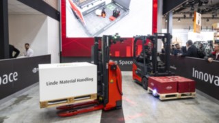 Dois equipamentos da Linde MH transportam mercadorias. Uma imagem digital dos equipamentos é visível num ecrã.