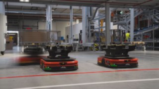 Três robôs móveis autónomos (AMR) da Linde MH circulam pelo armazém