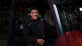 Um colaborador da Linde Material Handling está sentado num equipamento de movimentação de cargas e sorri para a câmara.