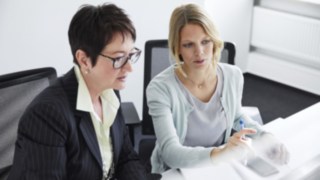 Colaboradora da Linde com uma jovem à secretária, em frente ao computador Colaboradora da Linde com uma jovem à secretária, em frente ao computador