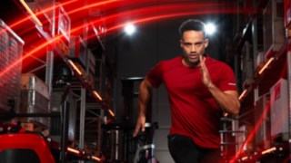 Um atleta corre num armazém, o empilhador retrátil Ri16 da Linde MH pode ser visto em segundo plano.