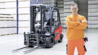 Os equipamentos da Linde transformam o trabalho numa experiência, oferecendo ao mesmo tempo o máximo de conforto e proteção. Um homem de braços cruzados num pavilhão de armazenamento. Um empilhador da Linde em segundo plano.