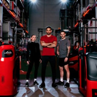 Uma mulher e dois homens, vestidos com roupa desportiva, estão num armazém, rodeados por equipamentos da Linde Material Handling.
