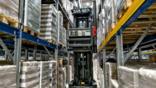 O empilhador para corredores estreitos automatizado Linde K-MATIC percorre um corredor de estanterias.
